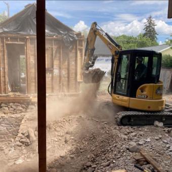 Compact excavator tearing down a small wood-framed structure